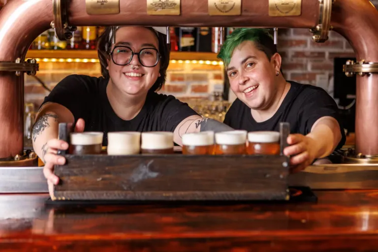 Dos mujeres sonrientes tras una cajón con varias jarras de cerveza