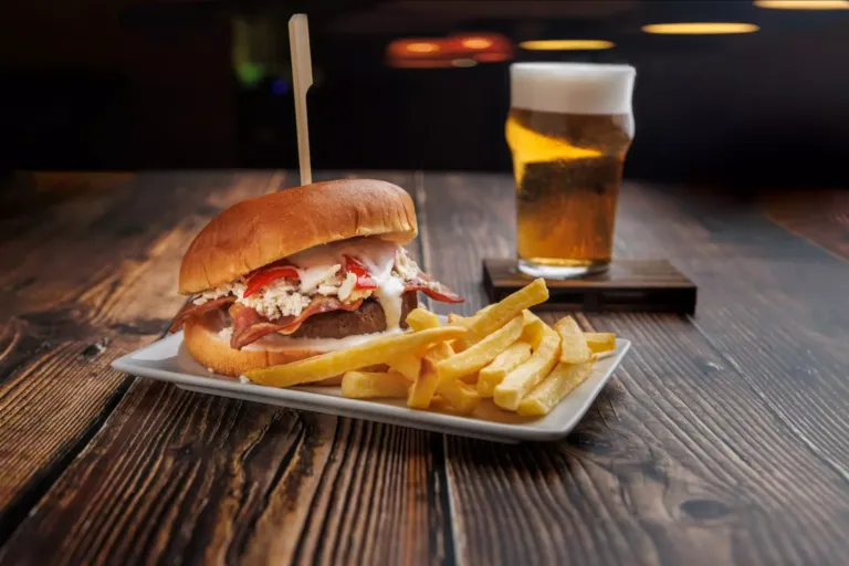 Hamburguesa con patatas fritas junto a una caña de cerveza