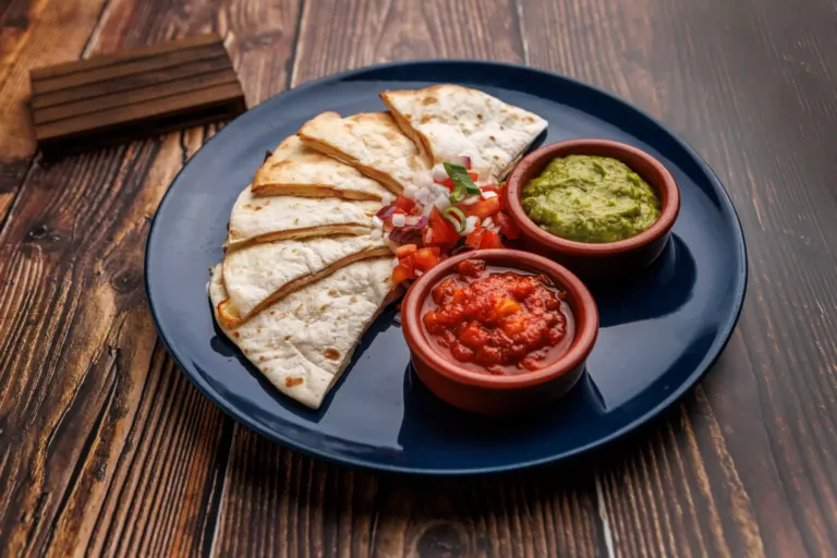 Plato con quesadillas de jamón y queso acompañadas de guacamole, salsa roja y pico de gallo