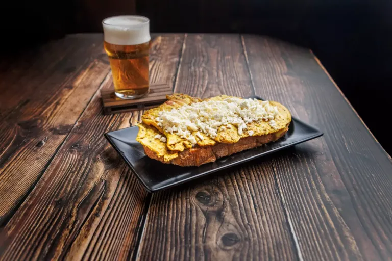 Tosta de pollo con pimienta y curry, queso de cabra y salsa de miel y mostaza junto a una cerveza